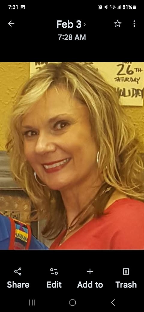Portrait of a woman with blonde layered hair and red lipstick, wearing a red and blue shirt, smiling at the camera